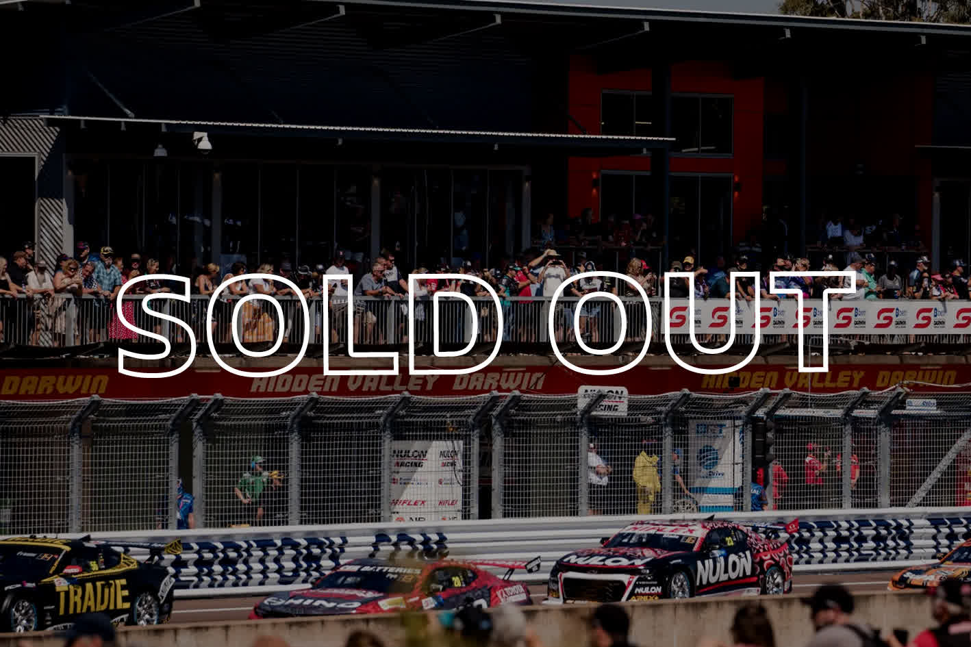 Race cars on a track with "SOLD OUT" text overlay; spectators watch from a packed grandstand at Hidden Valley Raceway.