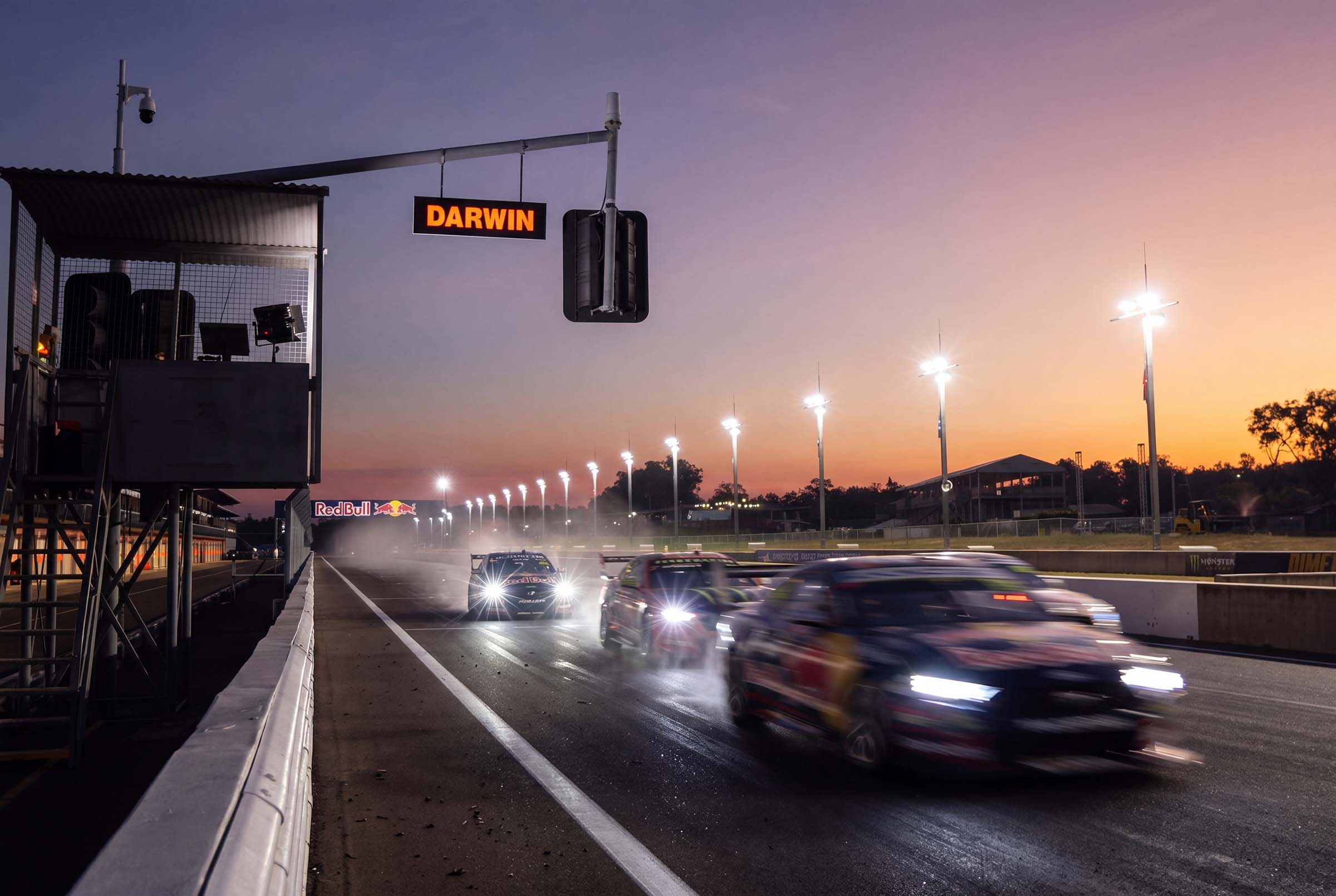 Supercars racing under lights at Hidden Valley Raceway in Darwin at sunset, with headlights shining along the track.
