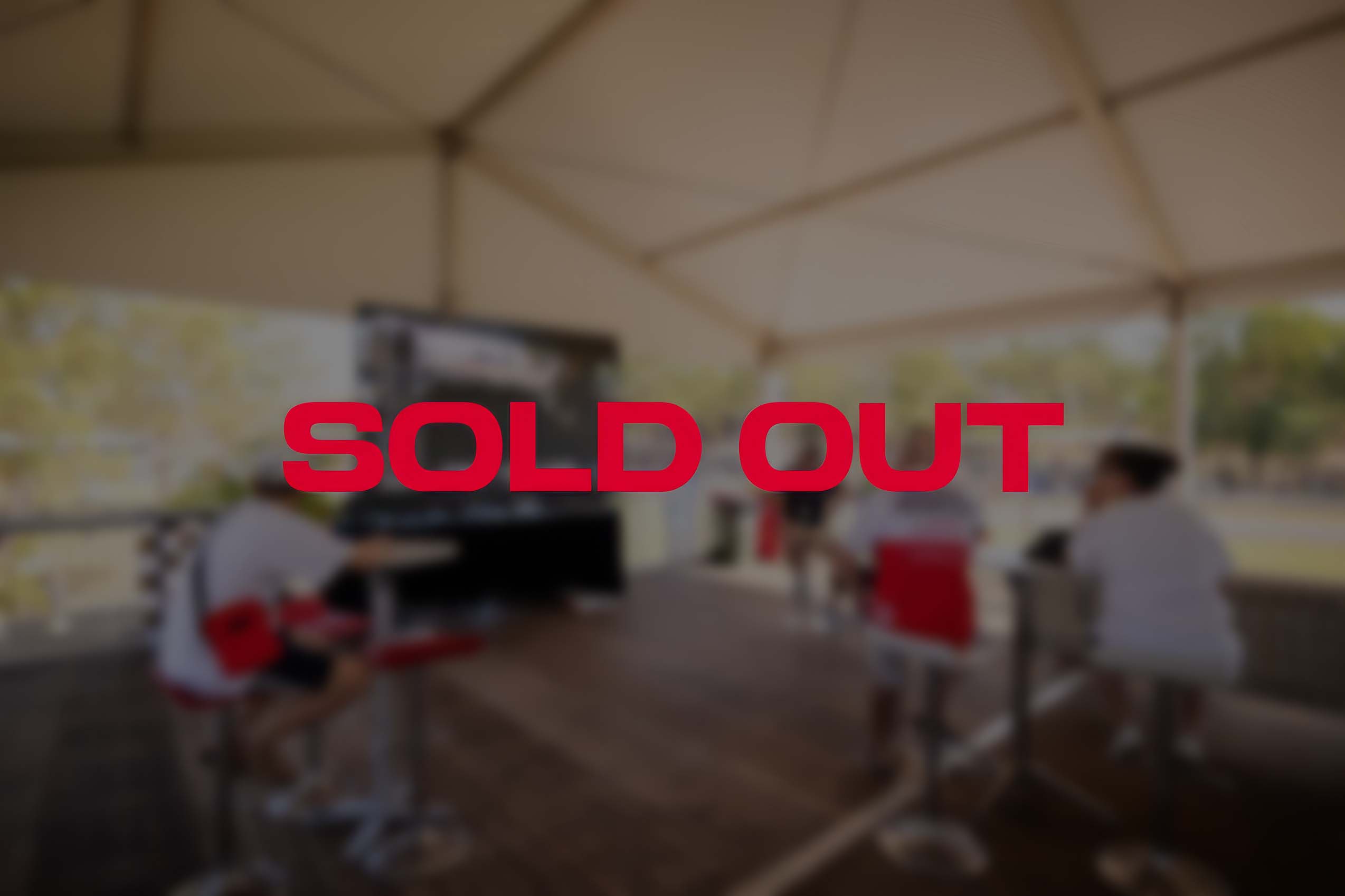 SOLD OUT text on top of blurred image of people sitting under a tent watching a large screen displaying a race, with trees visible in the background.