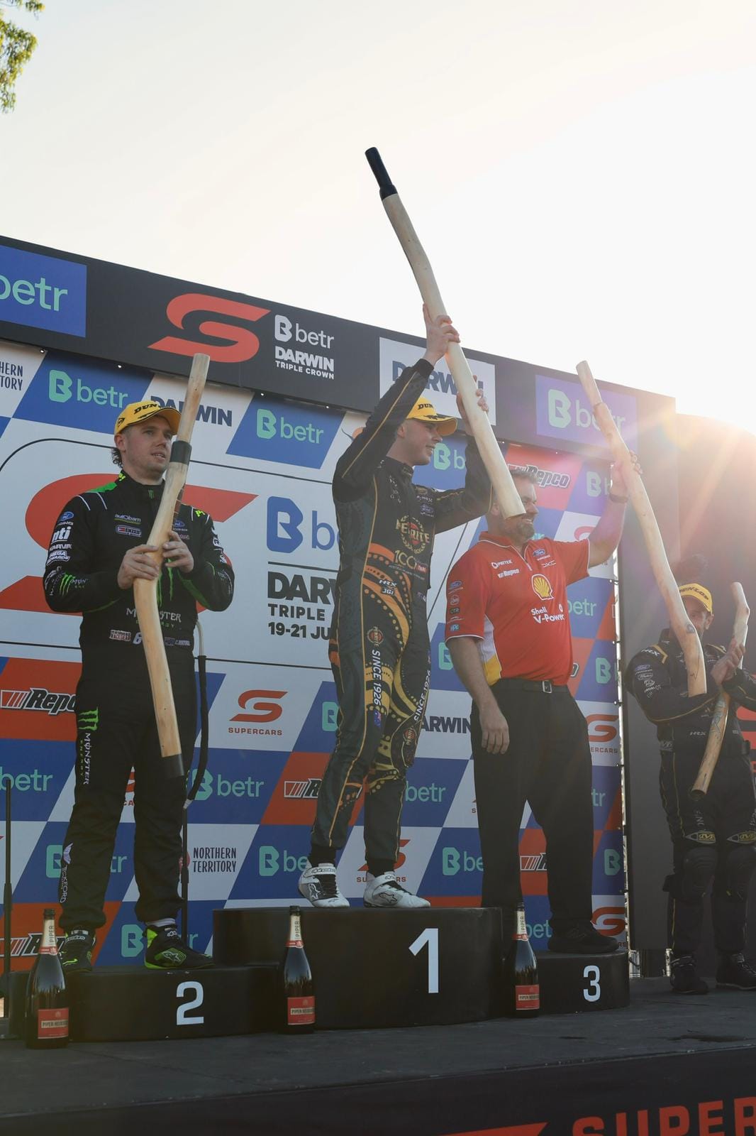 Supercars drivers celebrate on the Darwin Triple Crown podium while holding trophies.
