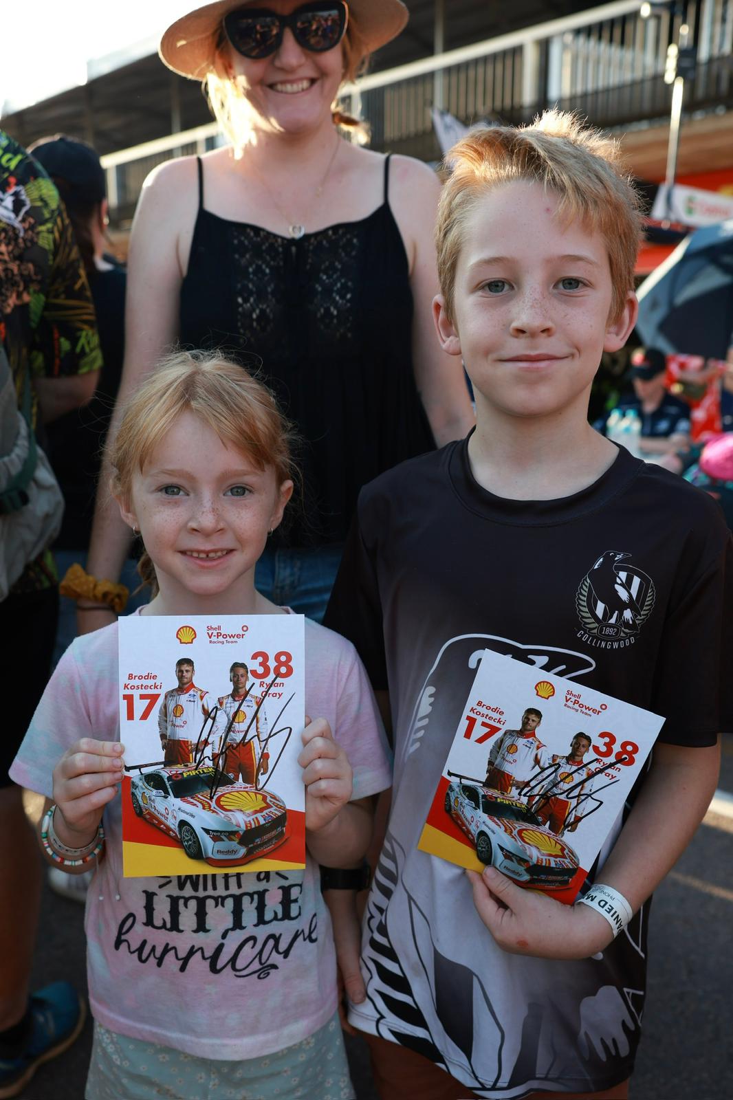 Two young fans hold signed Shell V-Power Racing Team posters while posing in the crowd at Darwin Supercars.