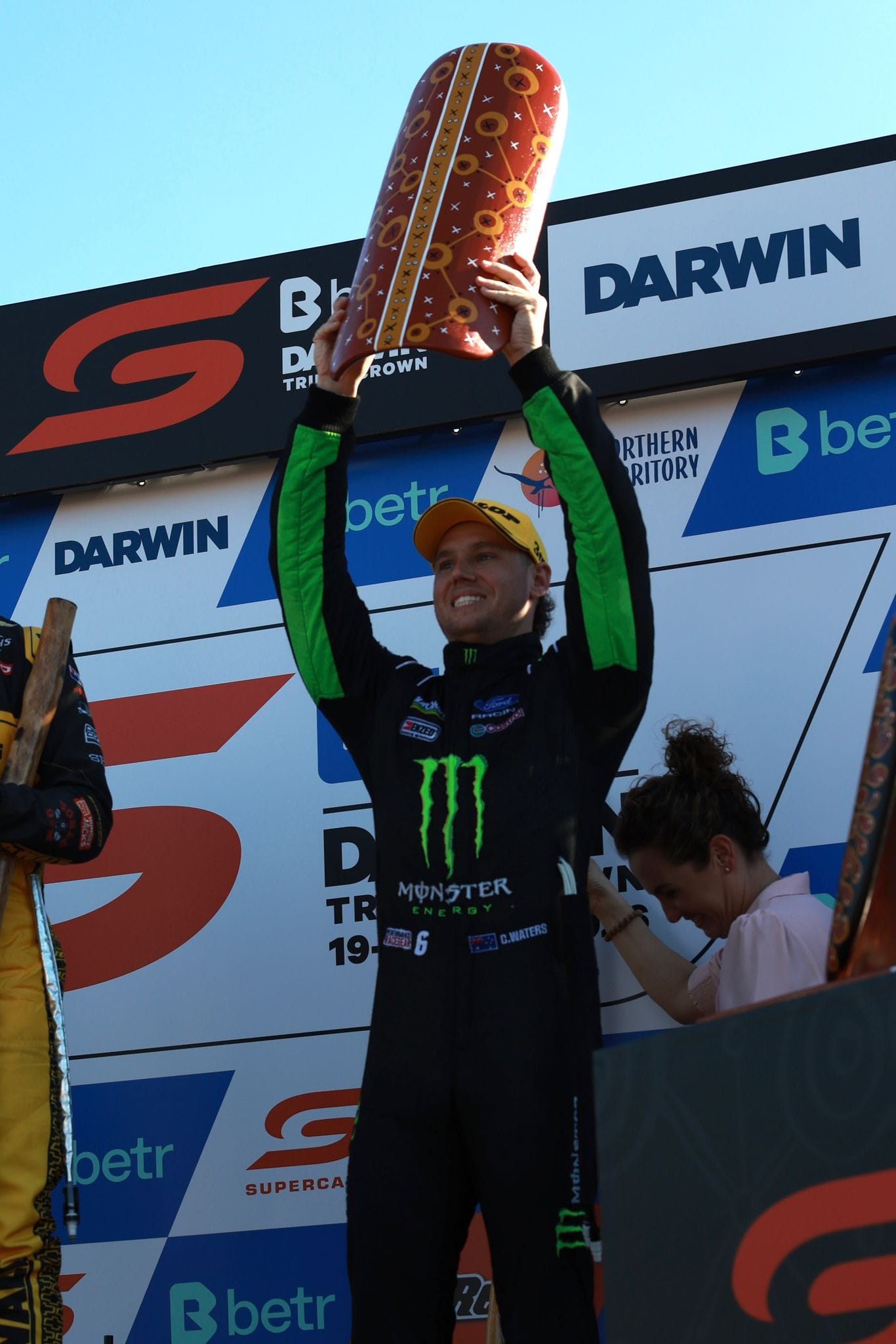 A Supercars driver lifts an Indigenous Round trophy above his head on the Darwin Triple Crown podium.