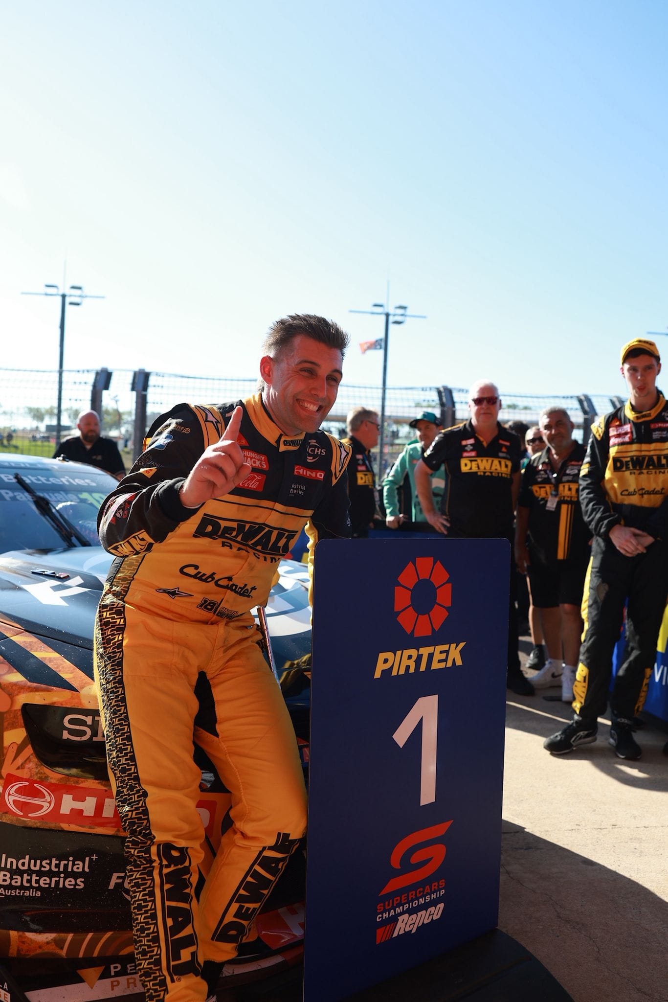 A DeWalt Racing driver celebrates beside his Supercar and first-place board after winning at Hidden Valley Raceway.