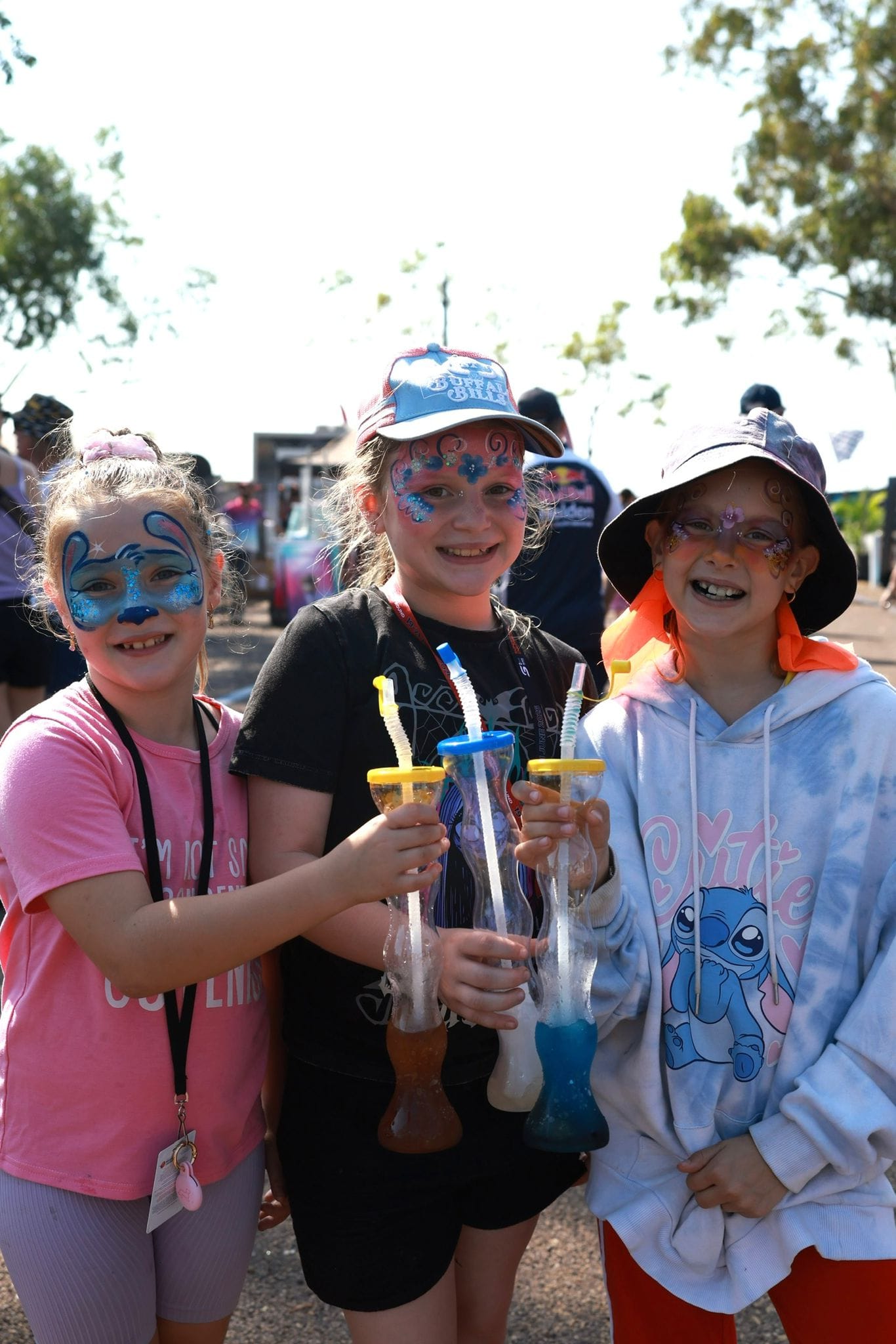 Three children with face paint smile while holding colourful drinks at Darwin Supercars.