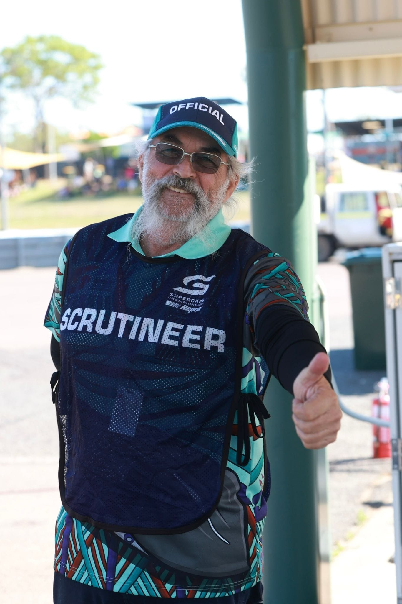 Man in an 'Official' hat and 'Scrutineer' shirt giving a thumbs up beside the track at Hidden Valley for the Darwin Supercars races