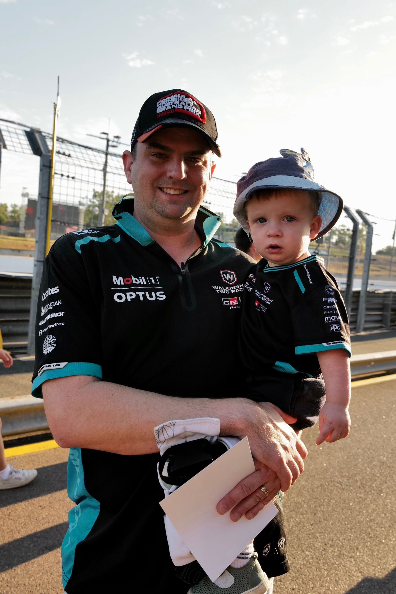 A smiling fan holds a young child dressed in team colours beside the racetrack at Hidden Valley Raceway during Darwin Supercars.