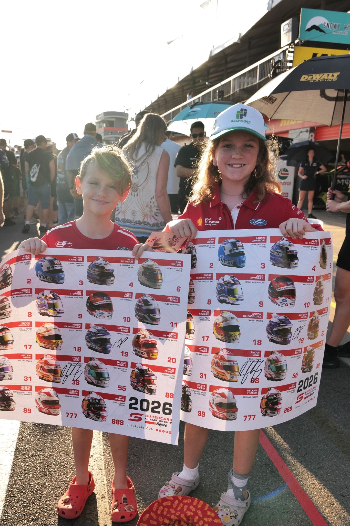 Two children proudly hold large signed 2026 Supercars Championship posters during a pit lane fan session at Hidden Valley Raceway.