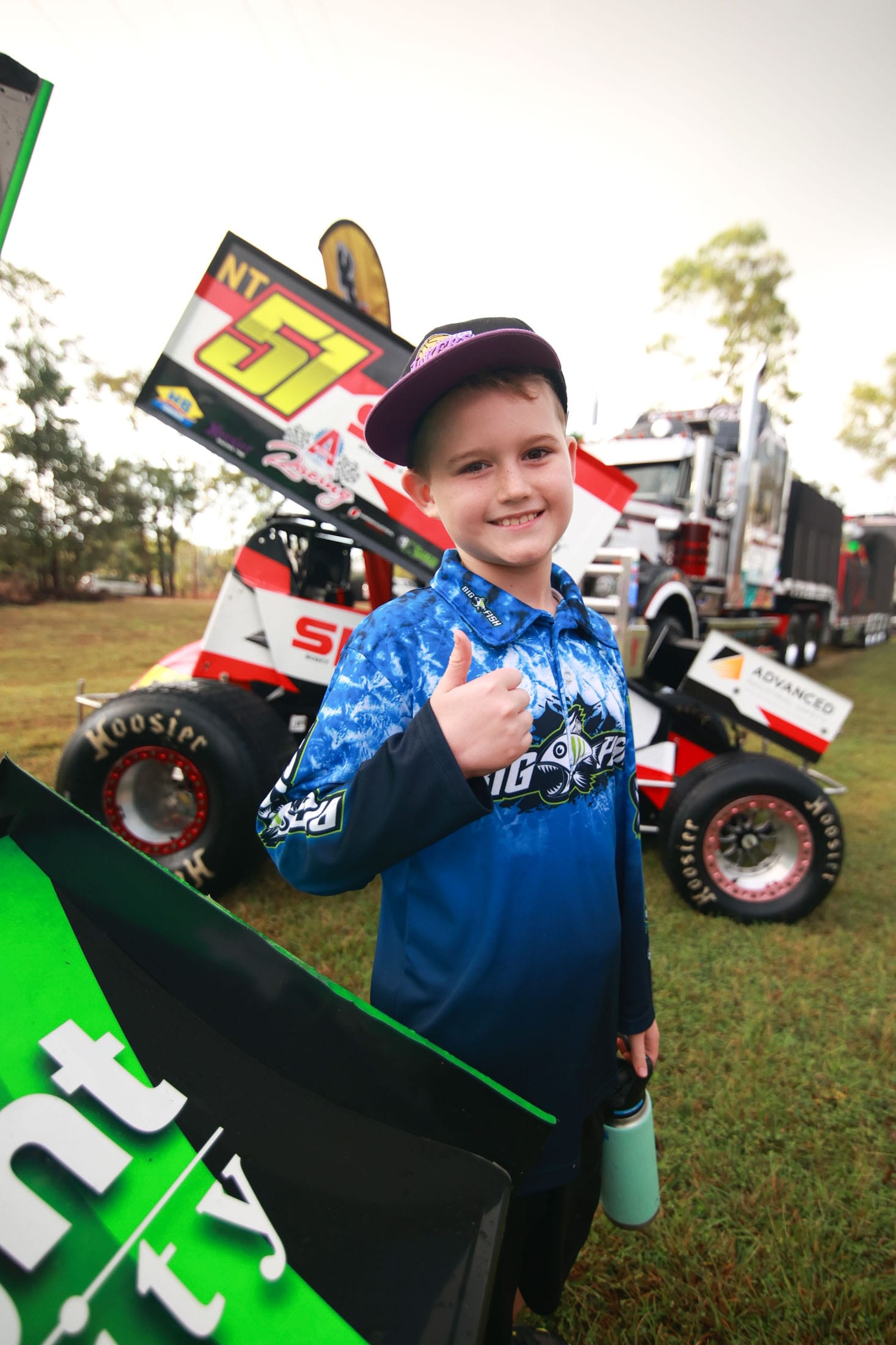 A young fan giving a thumbs up in front of a sprint car display at Hidden Valley Raceway.