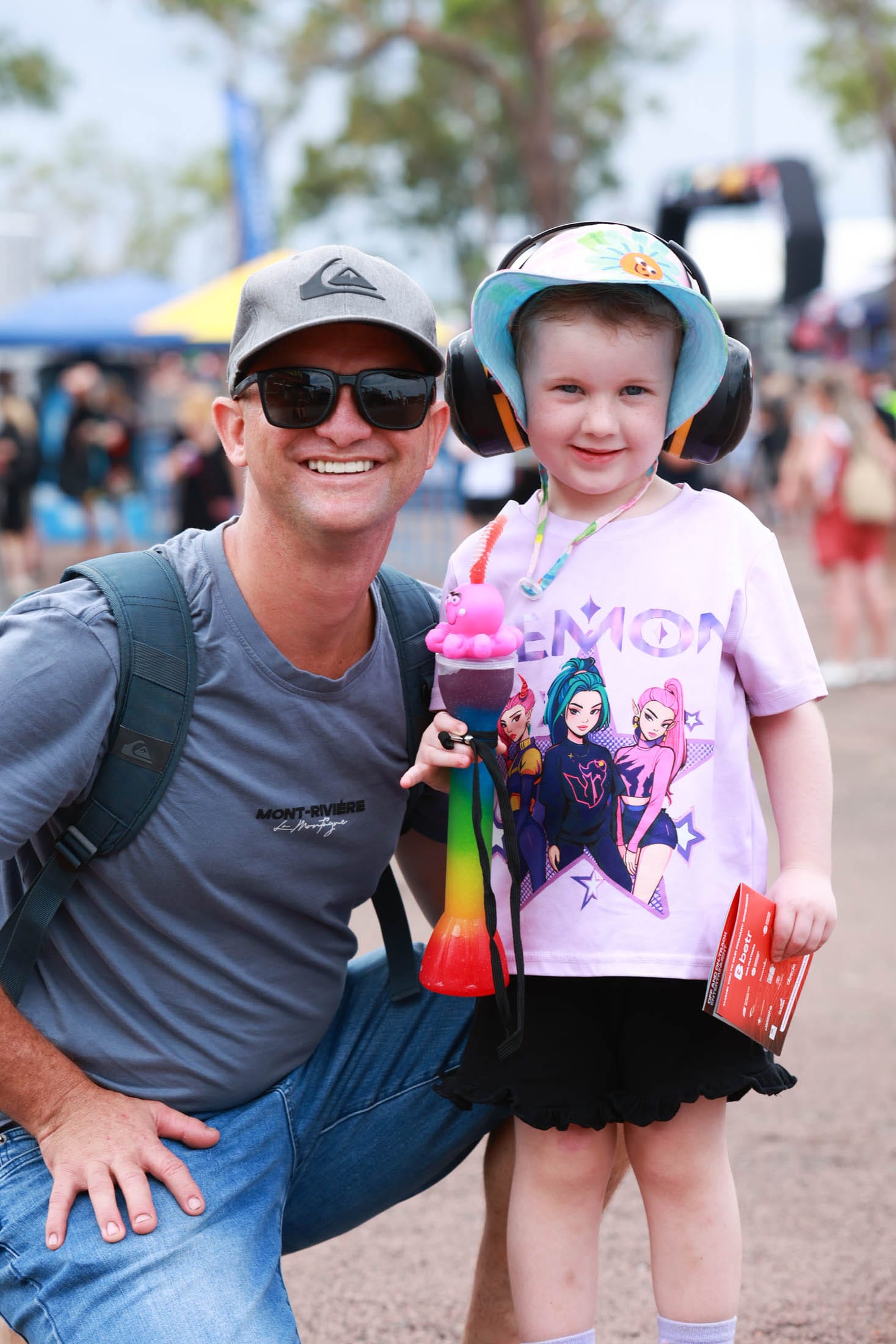An adult and child posing together in the Darwin Triple Crown fan zone, with the child wearing ear protection.