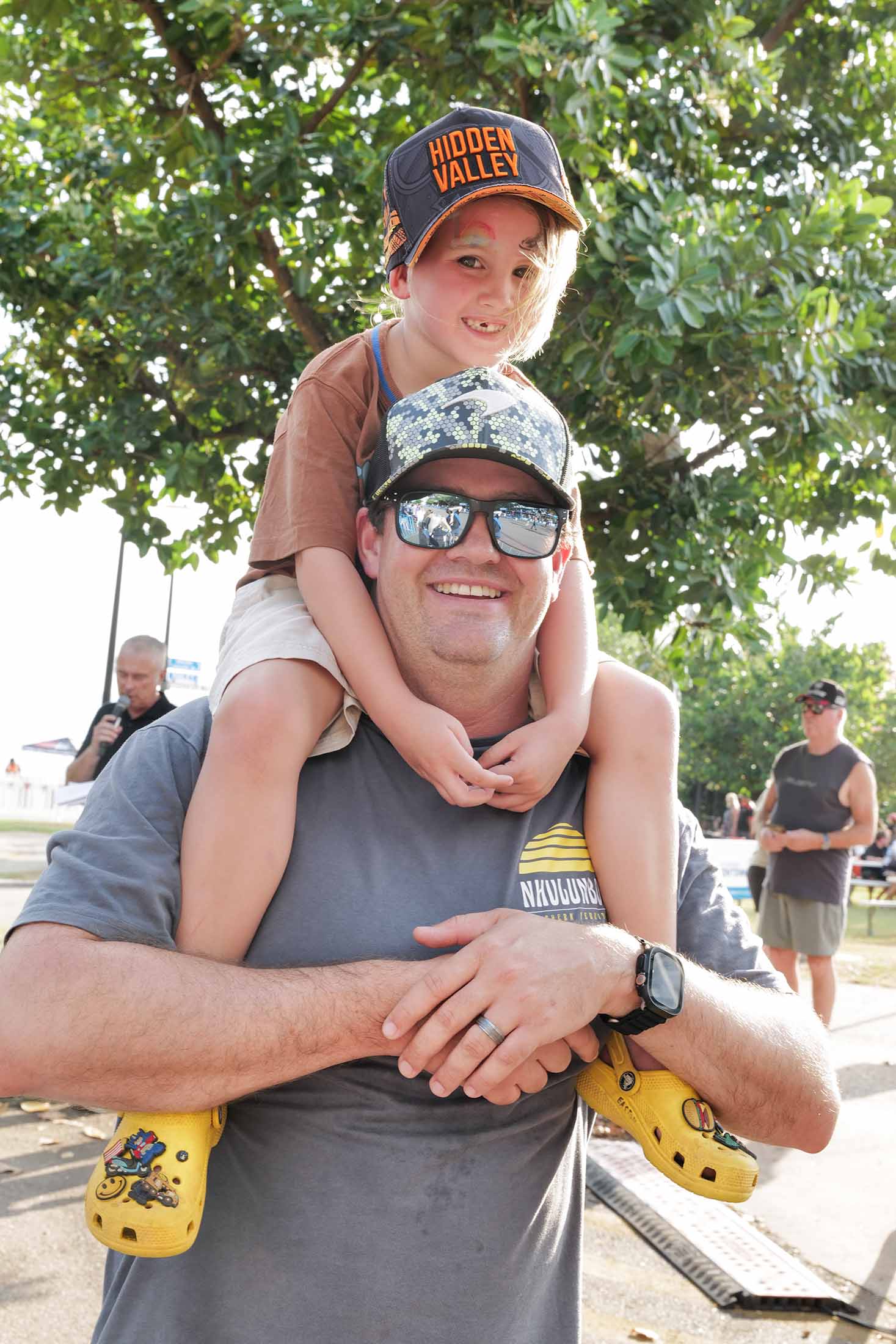 A child wearing a Hidden Valley cap sits on an adult’s shoulders at a Darwin Triple Crown Supercars event.