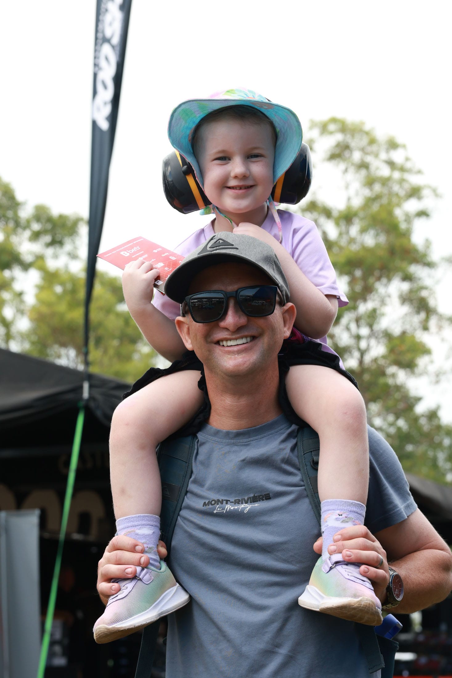 A child wearing ear protection sitting on an adult’s shoulders at the Darwin Triple Crown.