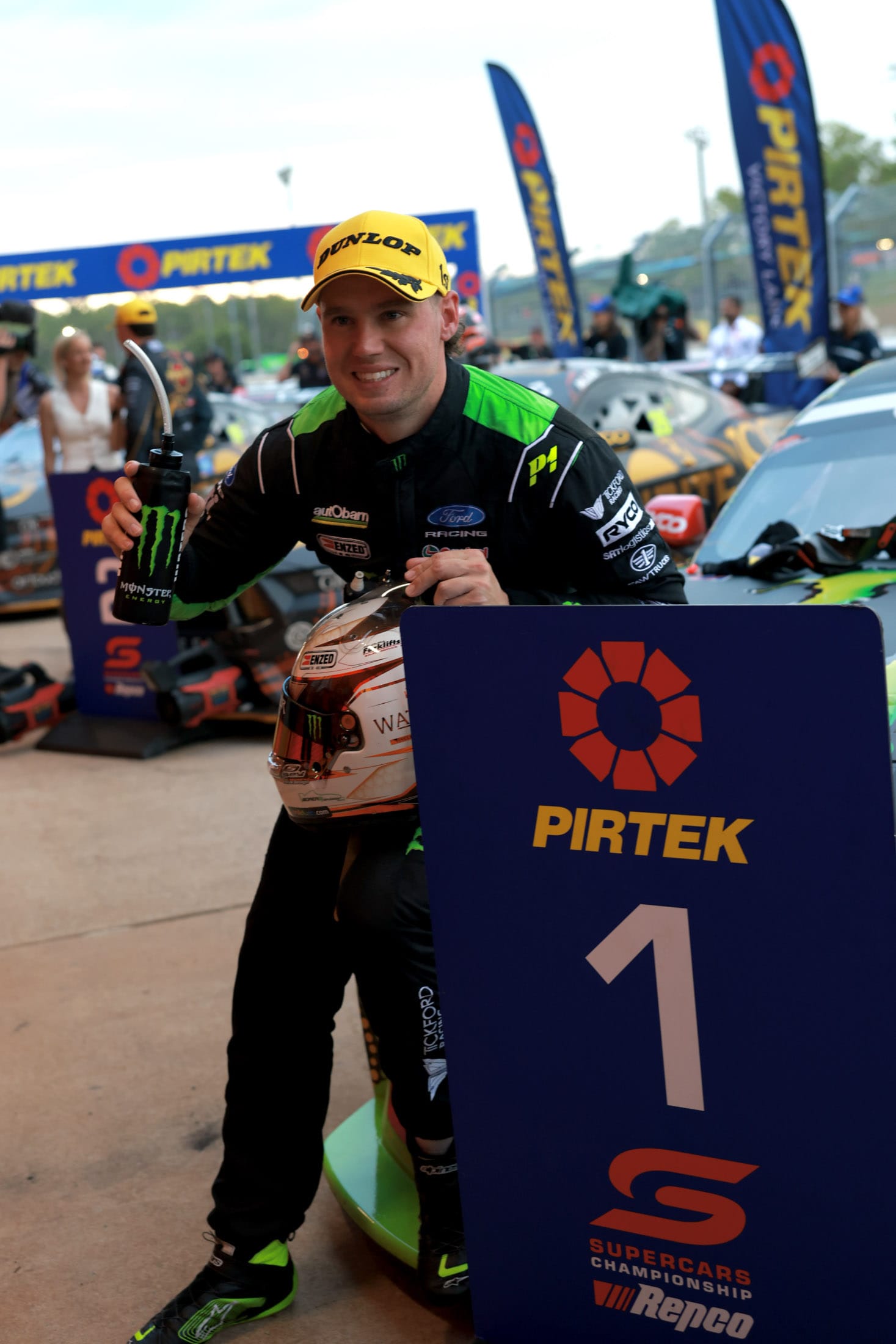 Monster Energy driver holding a helmet and drink bottle beside a Pirtek winners sign.