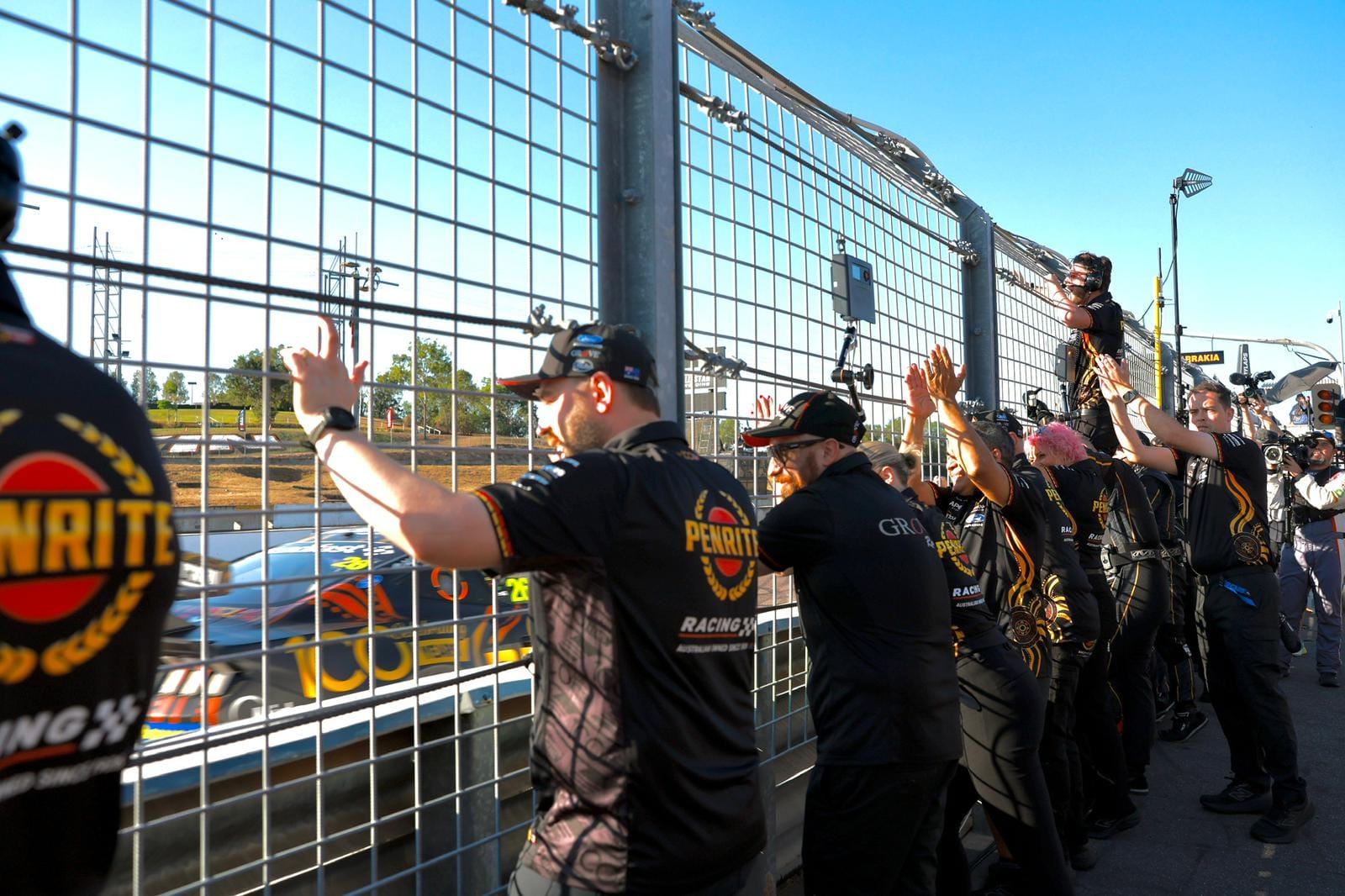 Penrite Racing team members cheer from behind the pit wall fence at Hidden Valley Raceway.