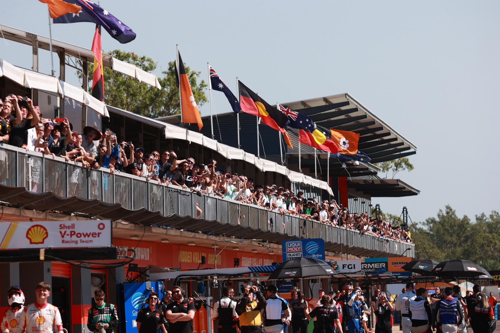 Crowds line the balcony above pit lane at Hidden Valley Raceway, with Aboriginal and Australian flags flying above the garages.