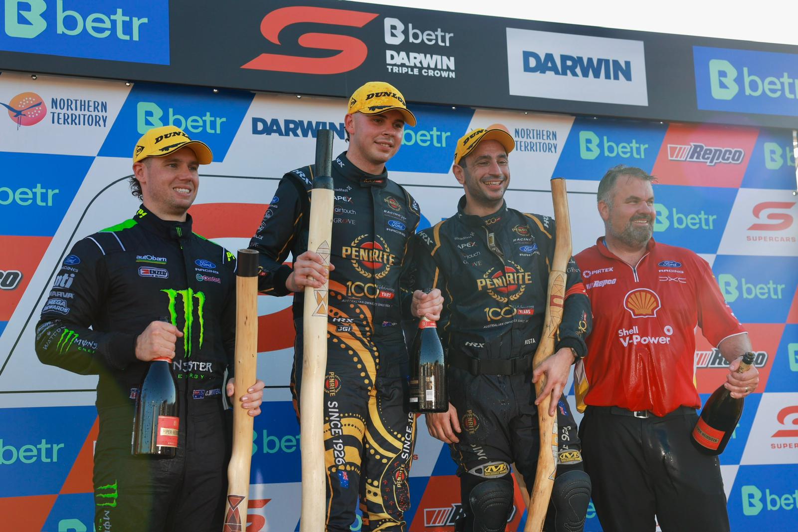 Supercars podium finishers and a team representative pose with trophies and champagne at Darwin Triple Crown.