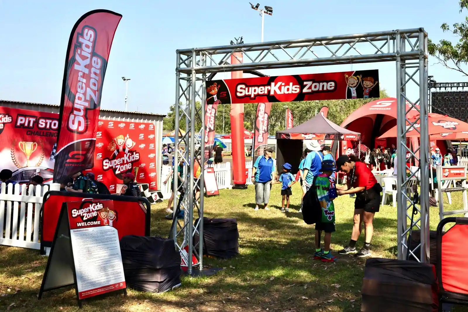 Entrance to the SuperKids Zone at an outdoor event, with banners, a welcome desk, and families entering the area.