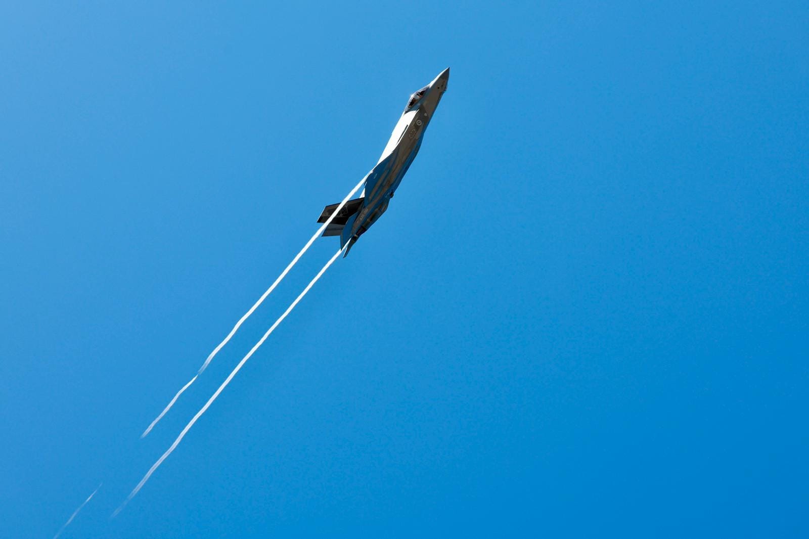 A jet climbs through a clear blue sky leaving white smoke trails during an aerial display at Darwin Supercars.