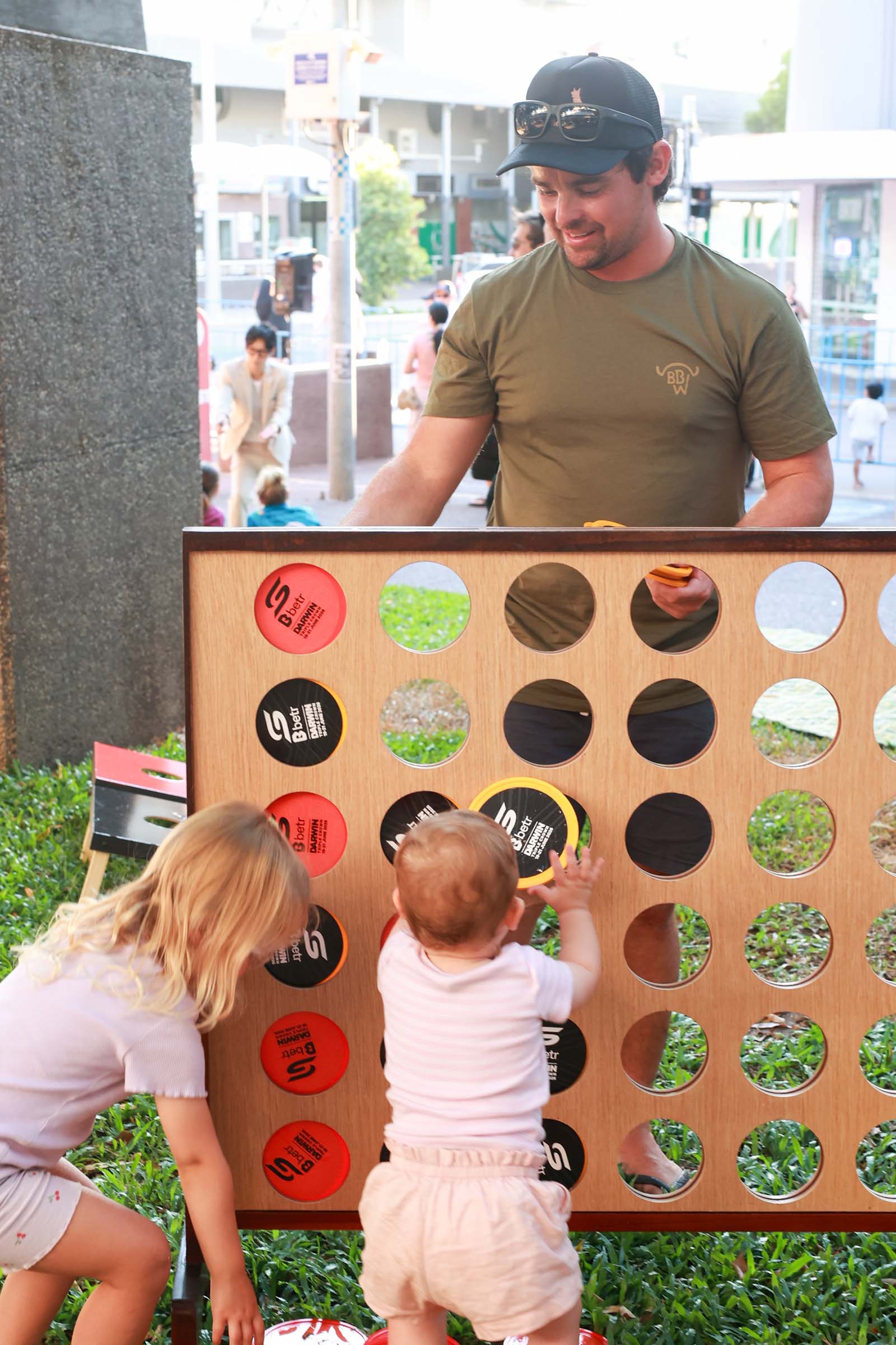 Children play with a man on a giant connect four game at a family activity area during the Darwin Supercars street event.