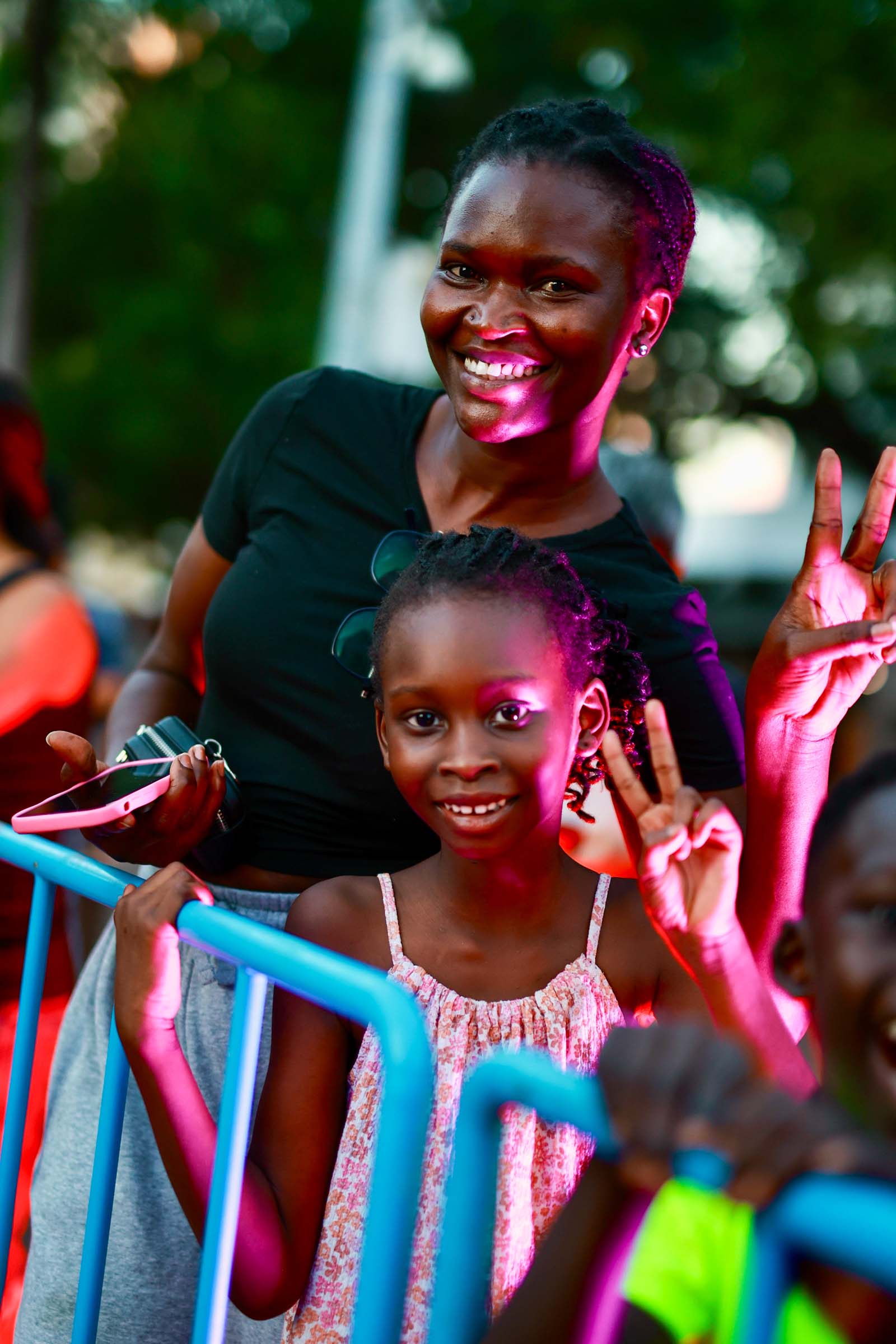 A smiling woman and child wave from behind a blue barrier at the Darwin Supercars street parade.