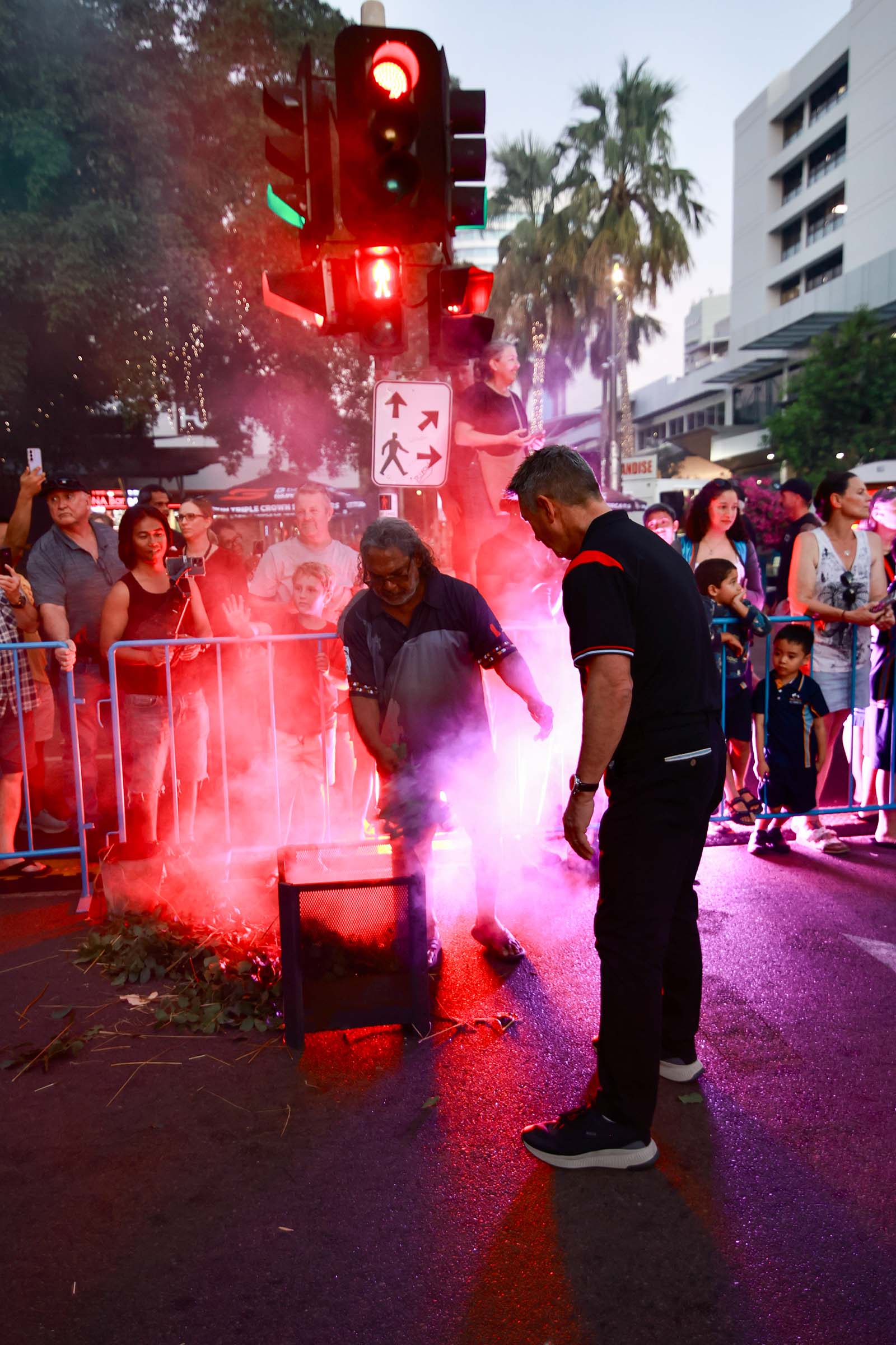 A smoking ceremony taking place on a Darwin street as spectators watch from behind barriers.