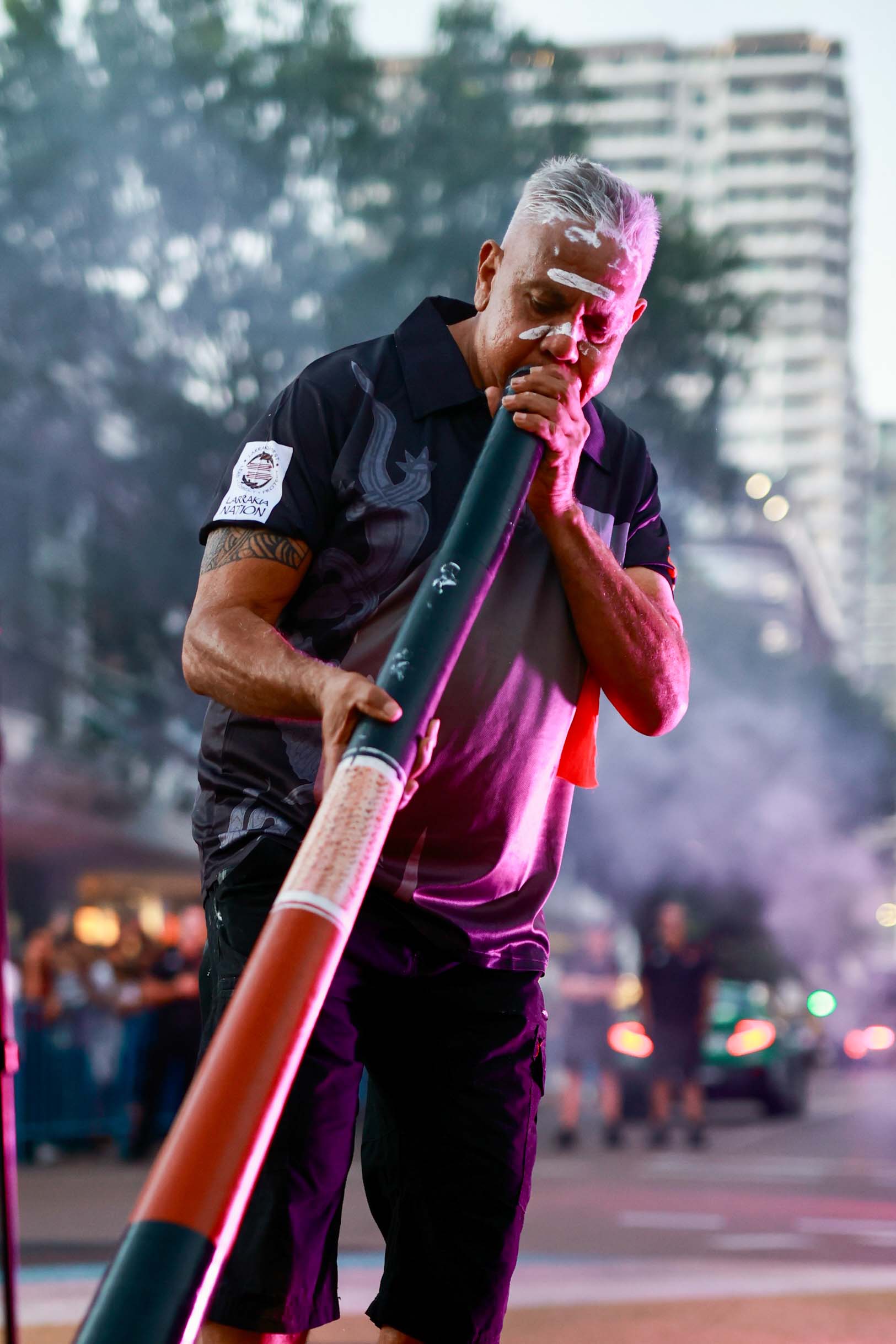 An Indigenous performer playing a didgeridoo during a smoking ceremony at the Darwin Supercars street parade.