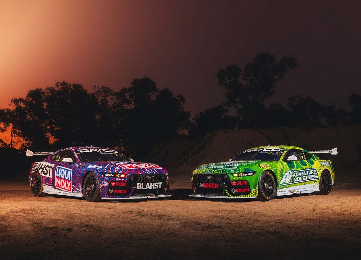 Two Blanchard Racing Team Supercars parked on dirt at night with trees silhouetted in the background.