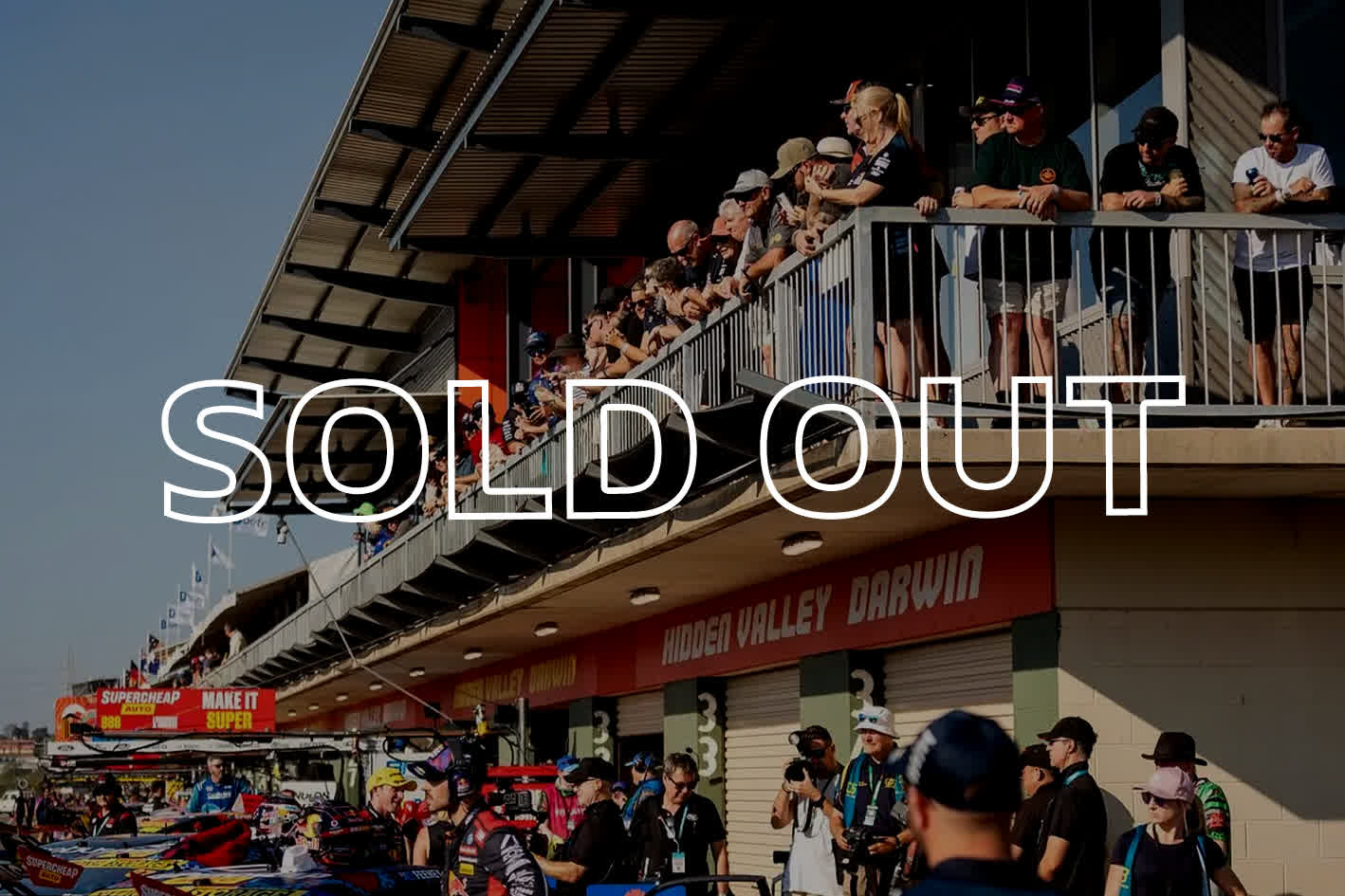 Crowd on a balcony at a racing event with "SOLD OUT" text overlay, overlooking cars and people below.