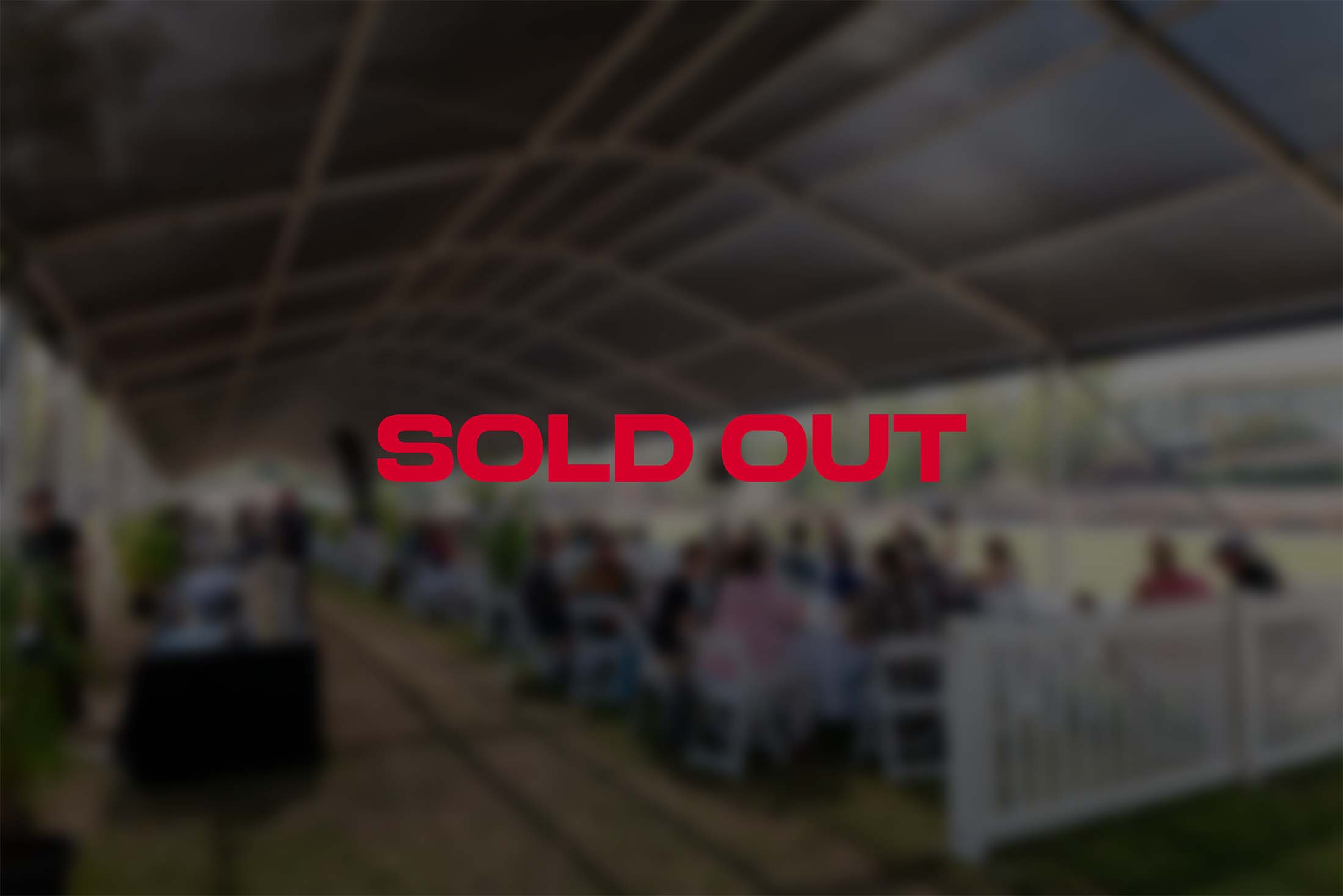 Red text showing SOLD OUT over the top of a blurred photo of people sitting in a shaded tent overlooking a race track